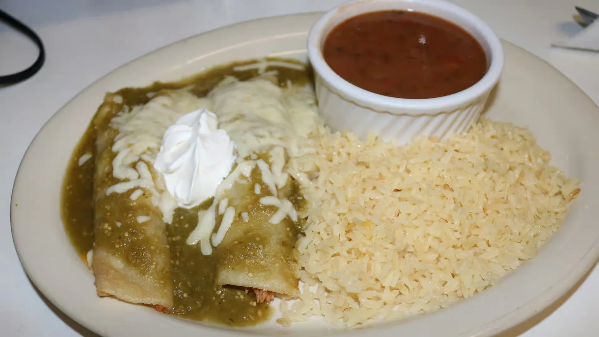 Green Enchiladas - Tender chicken enchiladas smothered in our signature tangy tomatillo green sauce, topped with sour cream and fresh cheese.